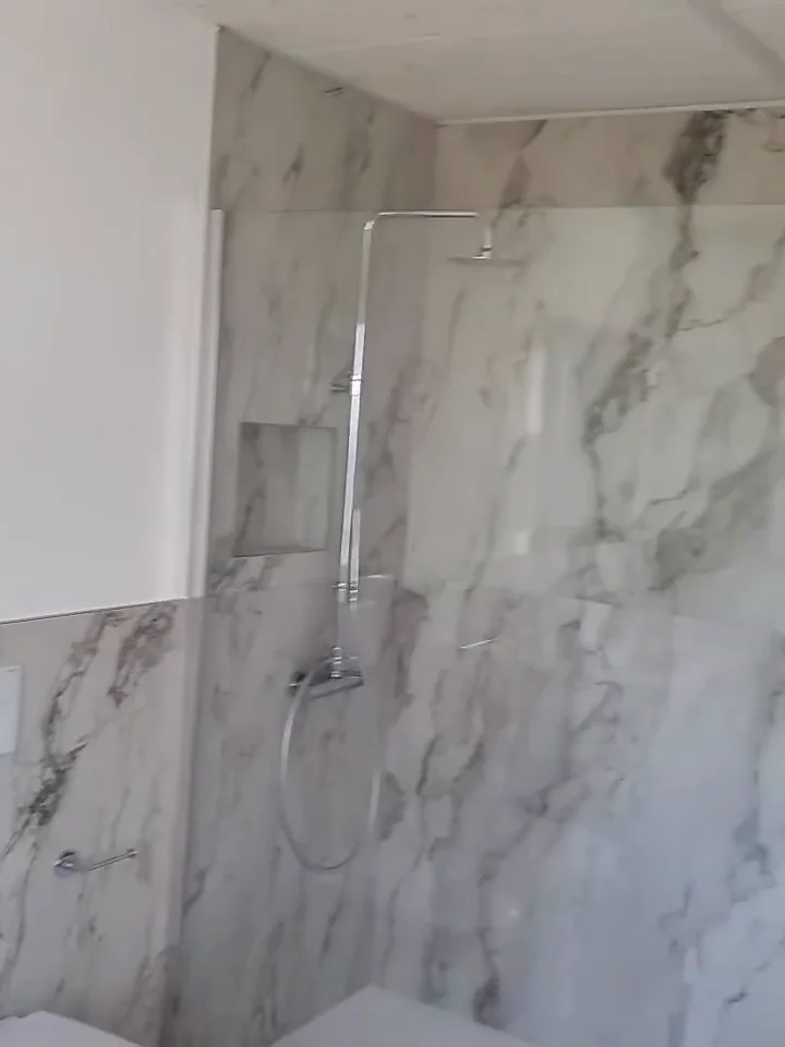 Bagno con rivestimento effetto marmo e doccia a vista