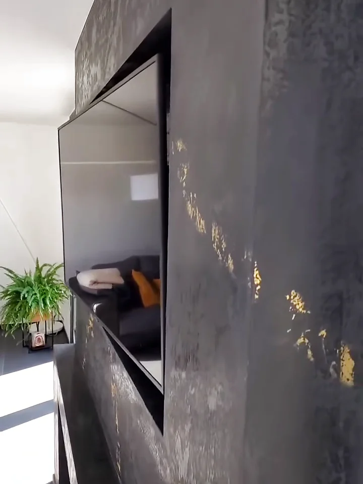 Parete in stucco materico con dettagli metallici e TV integrata